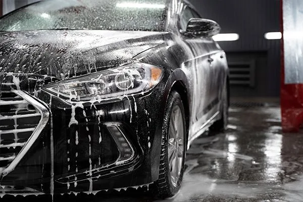 Black sedan covered in soap foam during a hand car wash