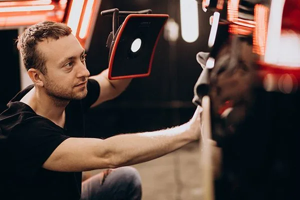 Detailer inspecting a car's paint under a work light