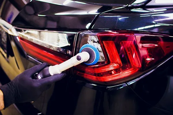 Detailer polishing a car taillight with a rotary foam pad