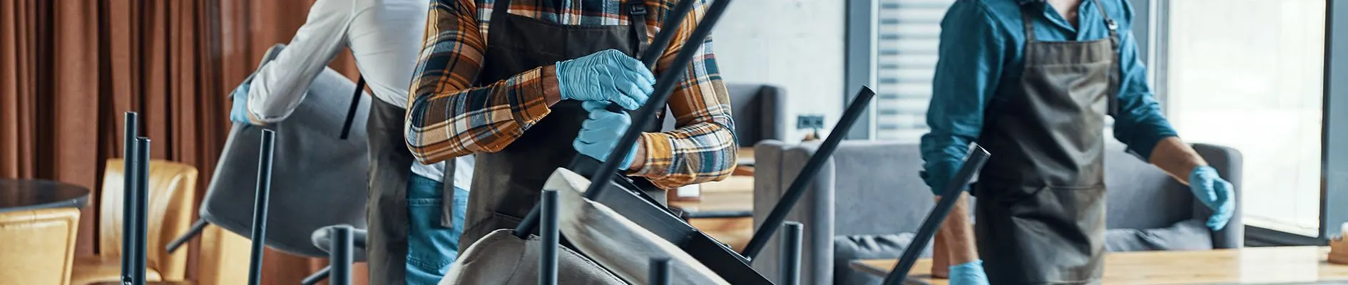 Crew in aprons and blue gloves stacking chairs while cleaning a commercial space