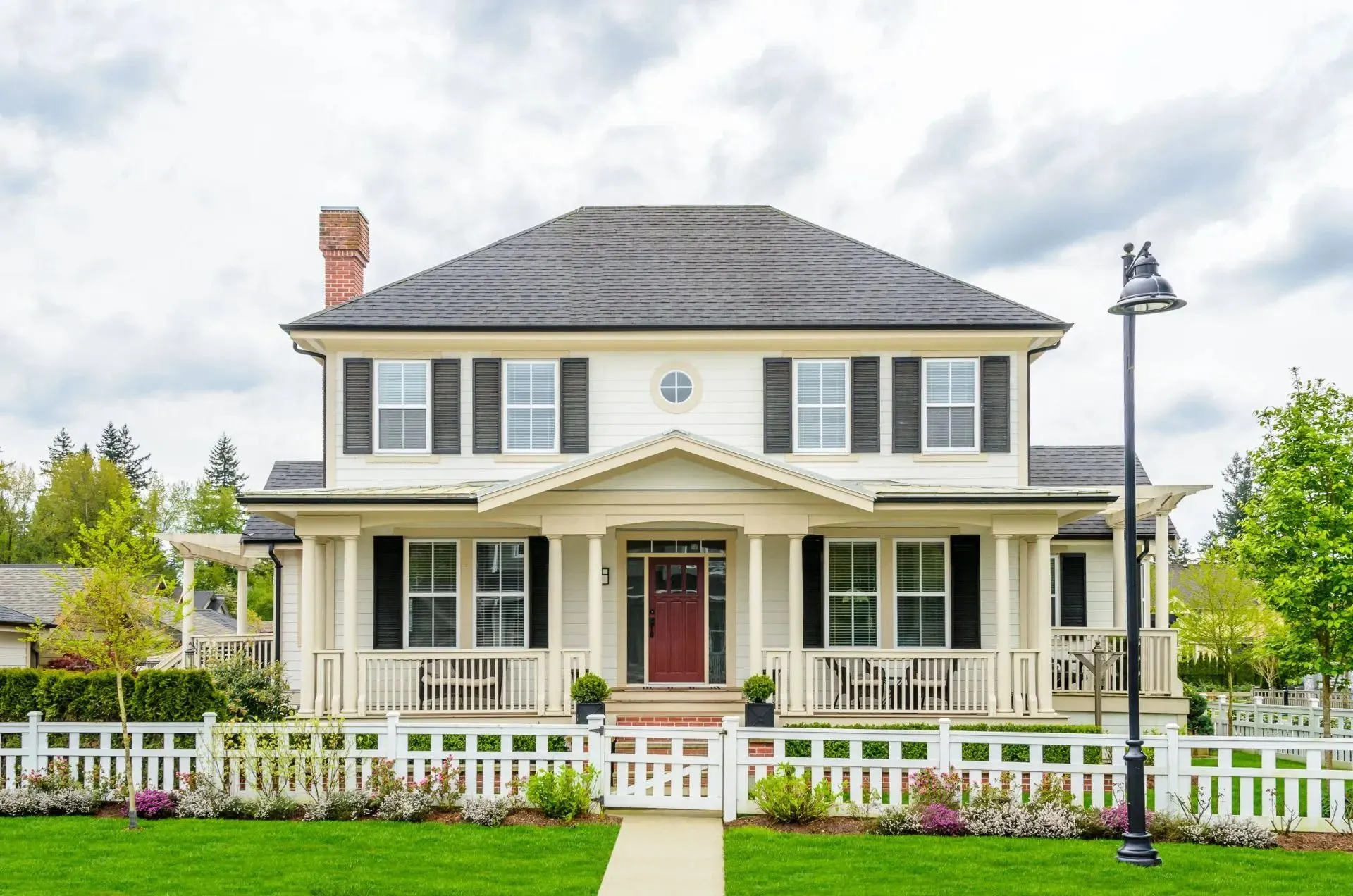 Two-story white colonial home with a covered front porch, red door, and white picket fence