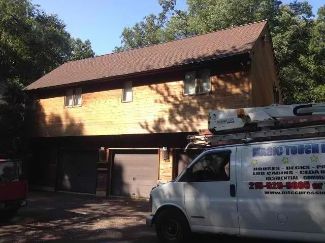 Two-story wood-sided home and garage after exterior painting, with a Magic Touch work van