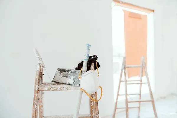 Paint-splattered ladders, putty knife, and dust mask in a freshly painted white room