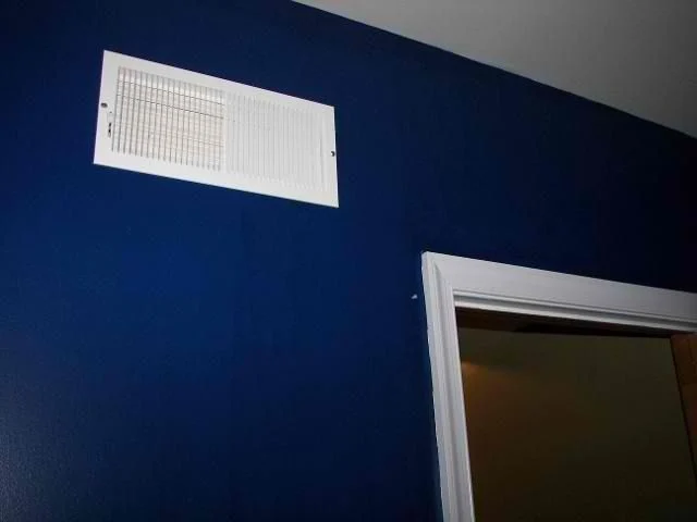 Navy blue painted wall with a white air vent and door trim