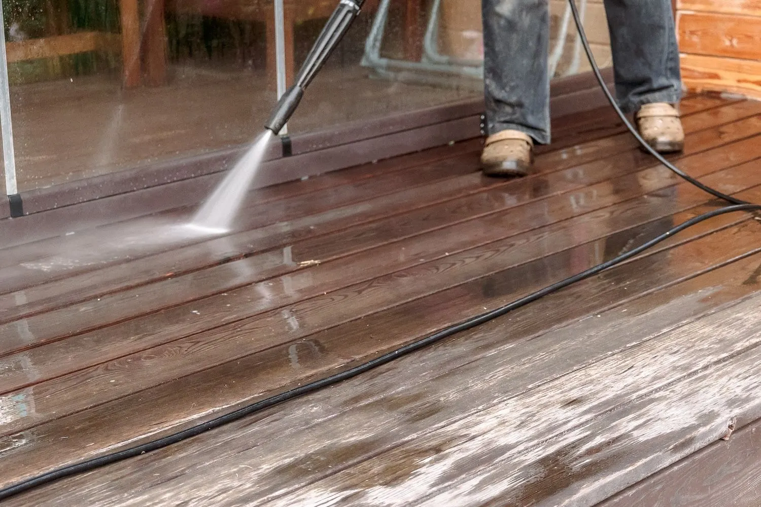 Pressure washer wand cleaning a weathered wood deck